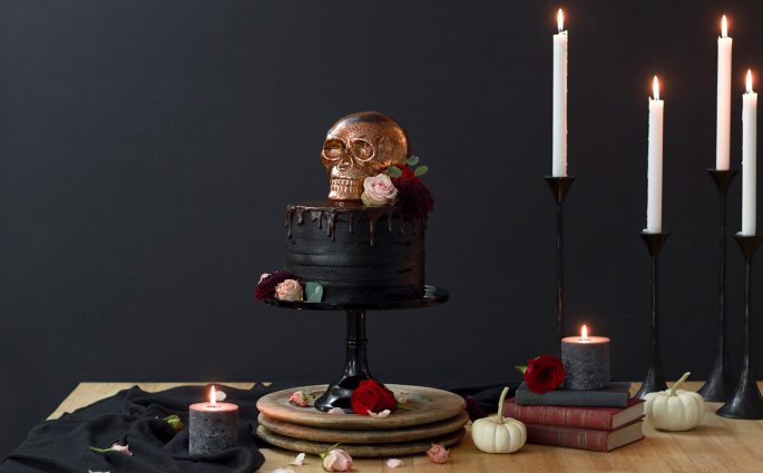 A Hauntingly Elegant Halloween Skull Cake. Cast a spell this Halloween with a hauntingly elegant skull cake. This naked cake topped with a dark chocolate drip is made with a rich dark chocolate cake and black chocolate buttercream frosting. Decorating perfectly with a stunning copper glass skull and fresh flowers. Recipe at www.designsofanykind.com