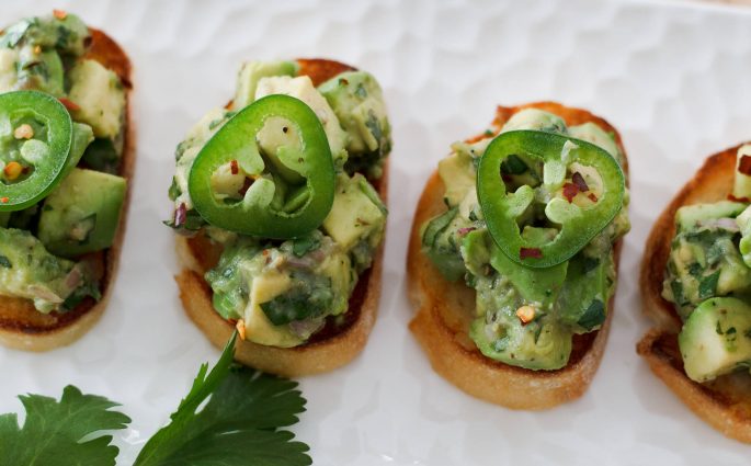 Delicious bruschetta topped with an aromatic mixture of avocados, herbs, garlic, and jalapenos. They are easy to make and perfect for a snack, appetizer, or tapas dinner. Recipe at www.designsofanykind.com